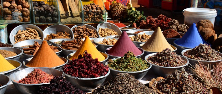 Cuencos con especias de colores en un mercado tradicional, incluyendo cúrcuma, pimienta, canela y hierbas secas